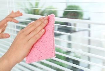 Person dusting wooden blinds with a microfiber cloth.